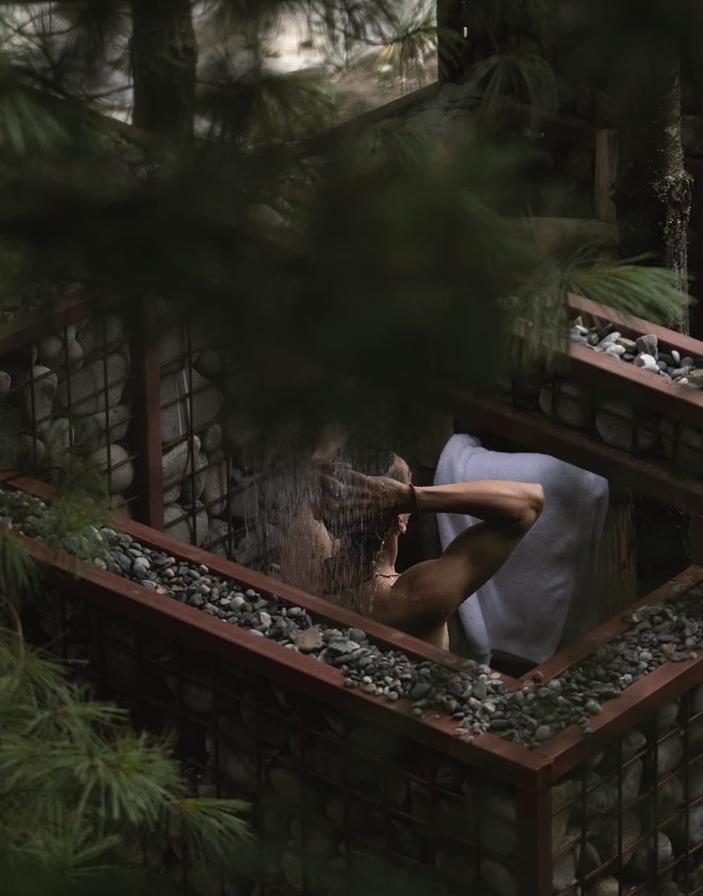 Guest showering in a gabion-walled outdoor shower among the pines
