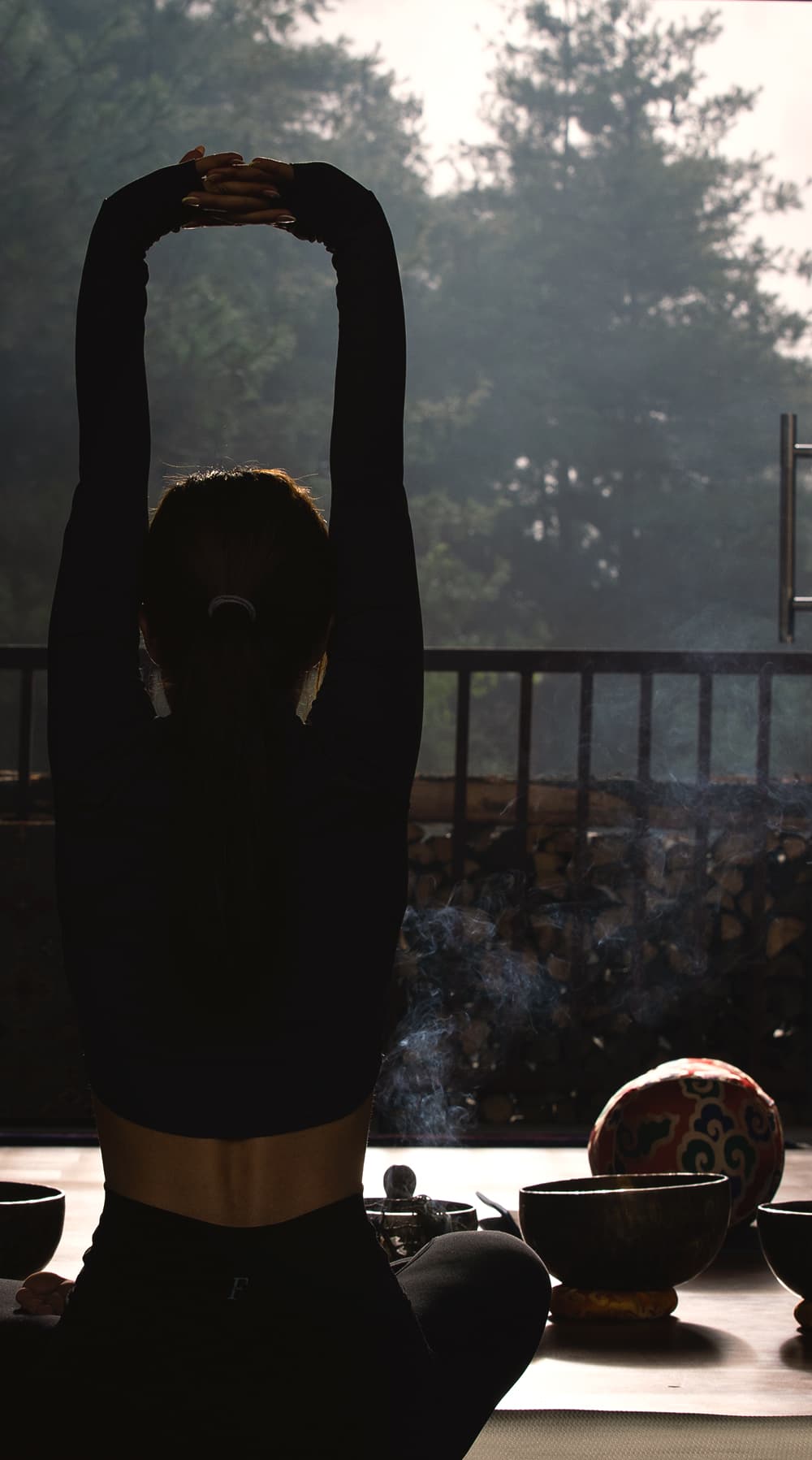 Guest stretching on a mat at sunrise with singing bowls on the deck