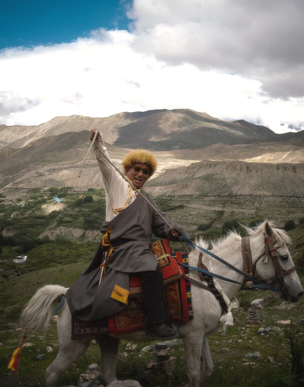 Rider in Tibetan dress on a white horse above the Mustang valley