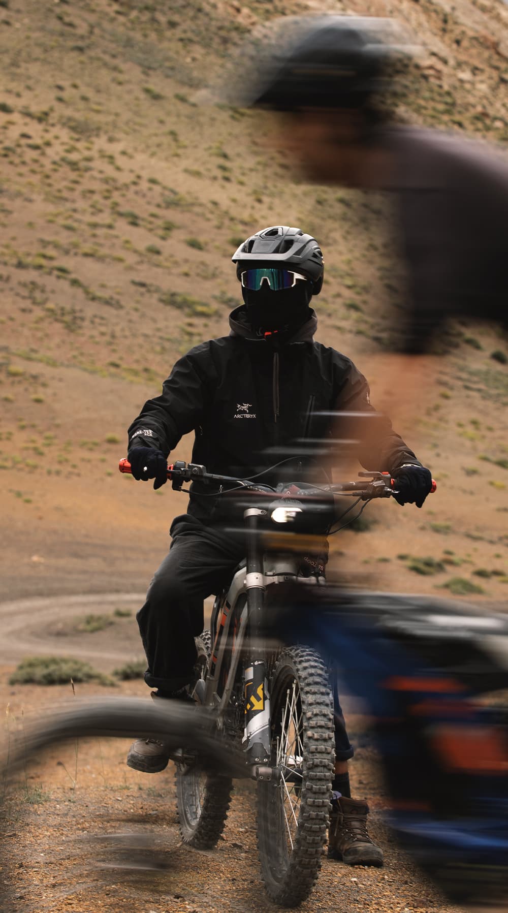 E-bike rider pausing on a desert trail as another rider blurs past