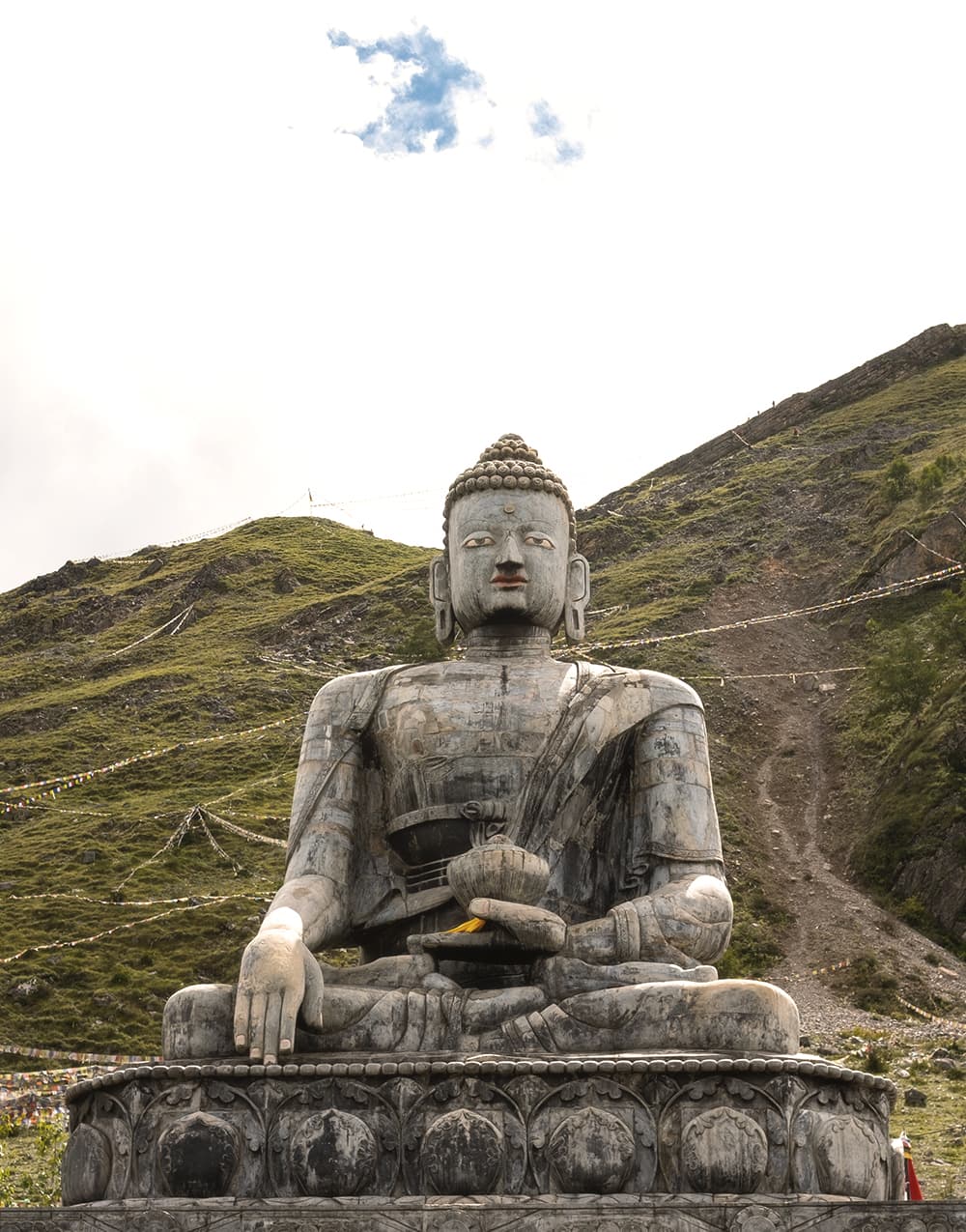 Stone Buddha statue seated below prayer-flag-strung hillsides