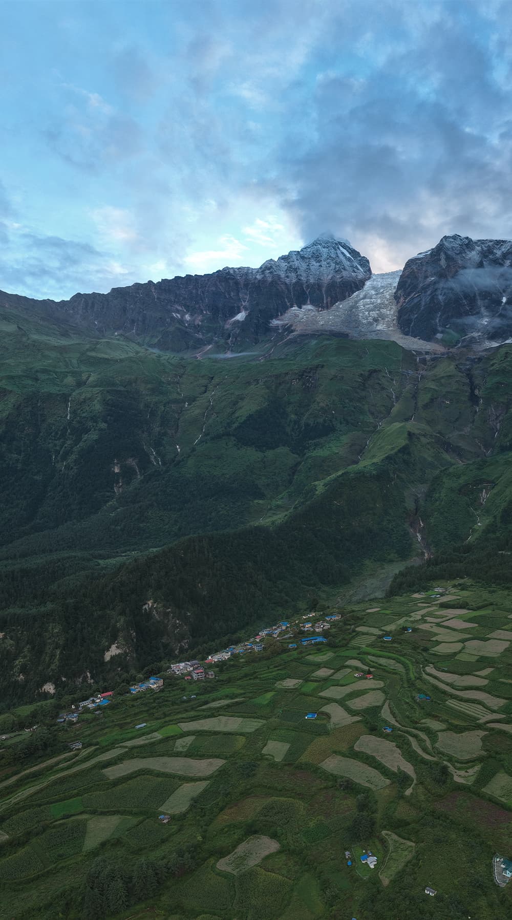 Terraced fields and village below a glaciated Himalayan wall at dawn