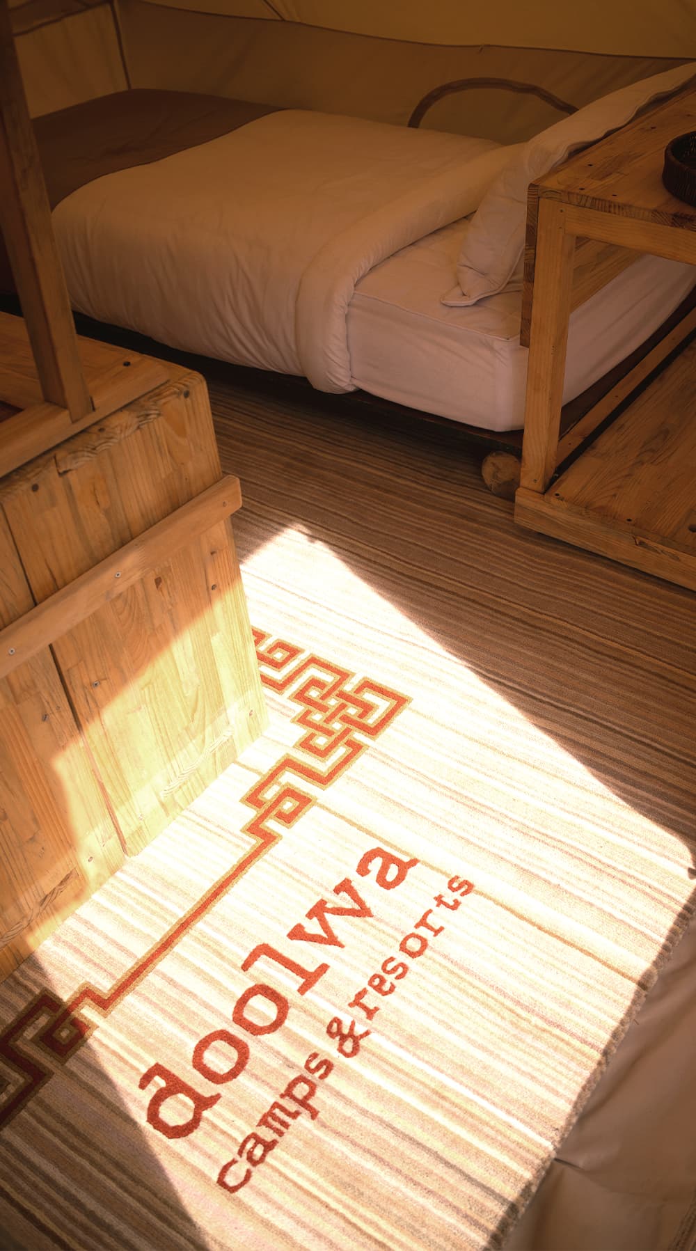 Sunlight falling across a Doolwa rug beside the bed inside a tent