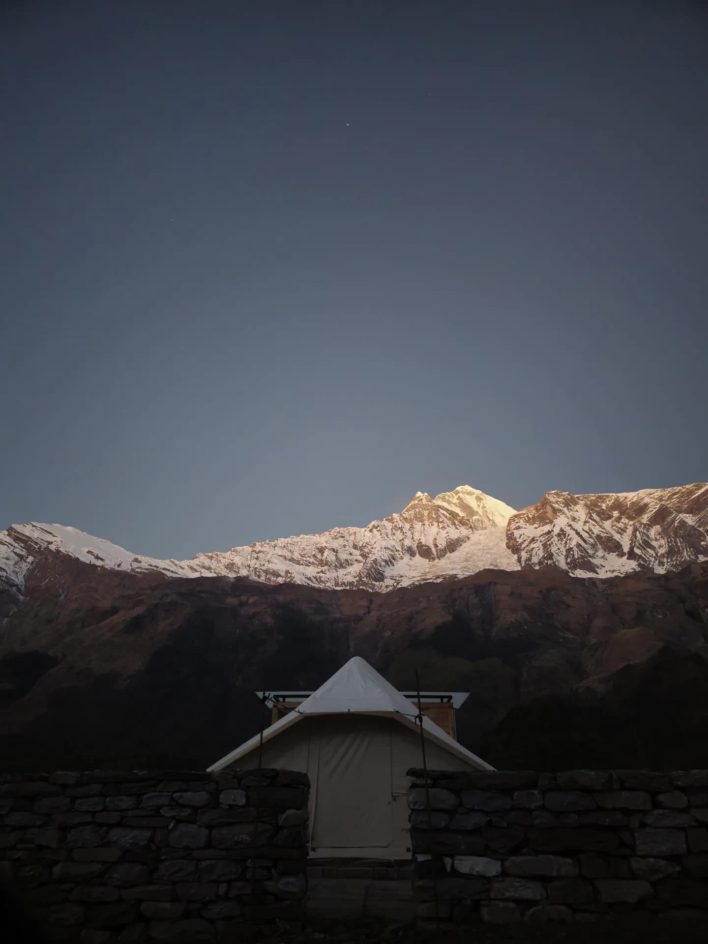 Heated glamping tent behind a stone wall below the Annapurna range